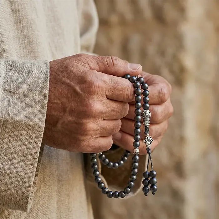 Hand holding a shaligram rosary 6mm with a blurred natural background