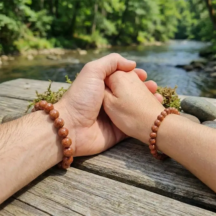 Pulseras de aventurina dorada en muñeca, cuentas marrón dorado con brillo natural junto al río | AuryStone