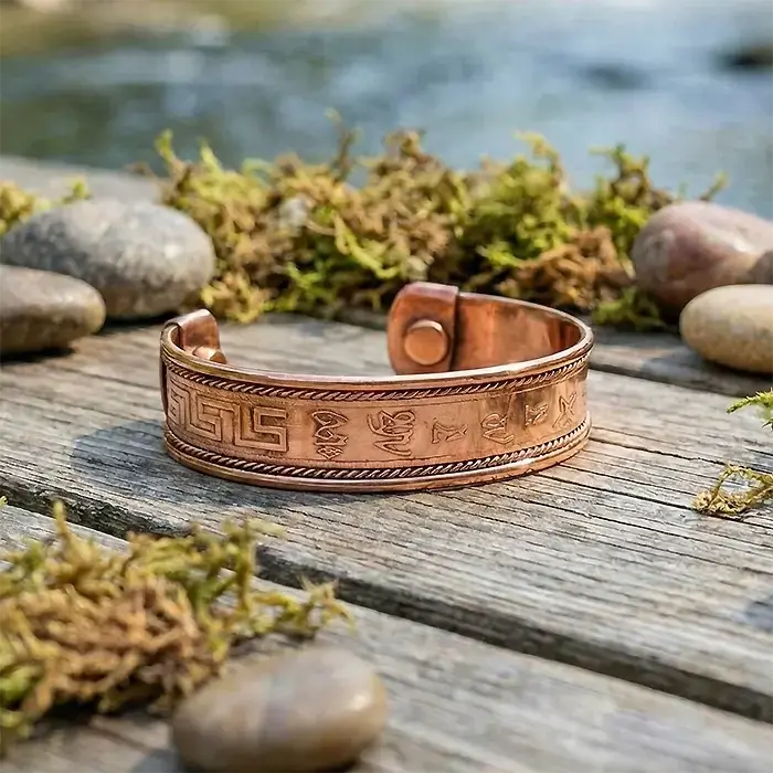 Copper bracelet with engraved patterns on a wooden surface with natural background